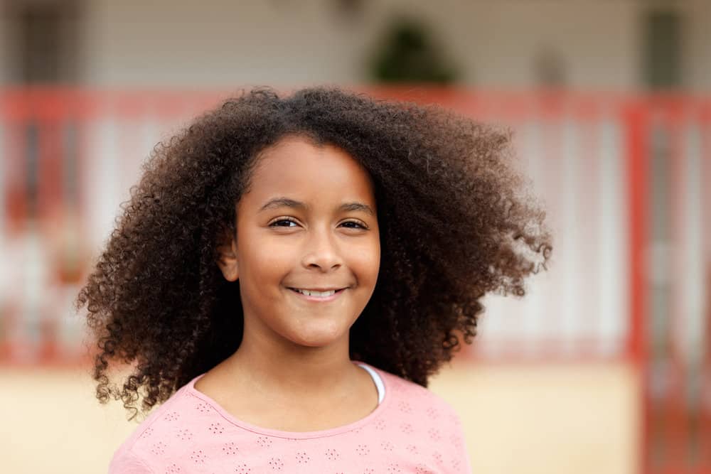 A beautiful young daughter with naturally thick hair is standing outside while her long hair blows in the wind.