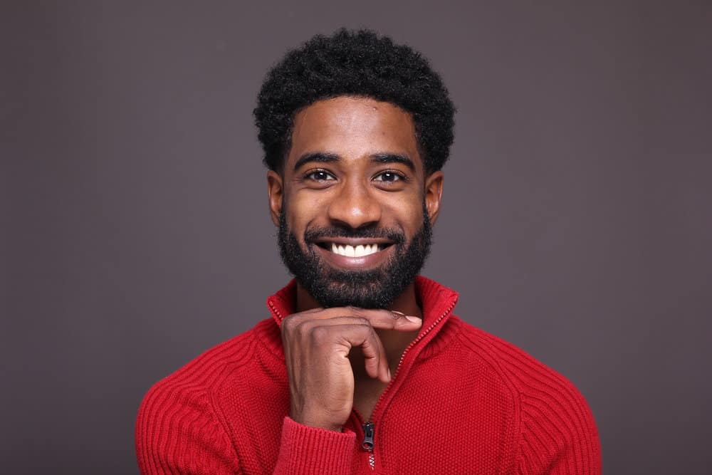 A black man with a patchy beard keeps his skin hydrated and massages his face to affect beard growth. 