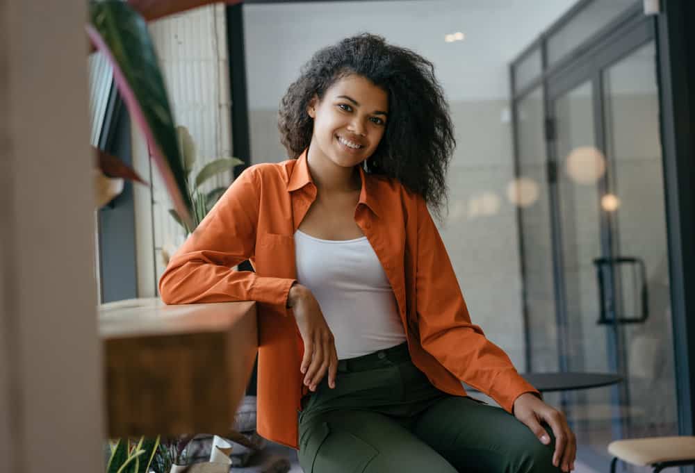 A black woman with a cute smile is wearing a casual shirt made from mulberry silk fibers to protect her hair strands.