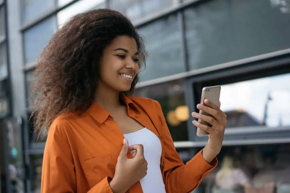 Satin vs. Silk for Hair: What Is Better for Your Hair? 6 A lady that's reading an article on her mobile phone about whether silk pillowcases or satin pillowcases are better.