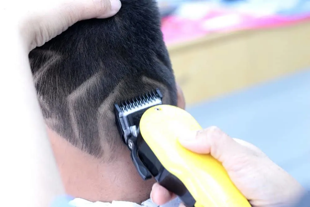 A young boy is getting a fresh, new look with a double-line haircut, adding sharp edges to his naturally short hair.
