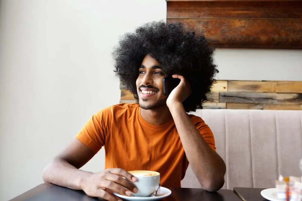 How to Make Your Hair Grow Faster and Thicker as a Black Man 9 An African male talking on the phone to a friend that has been experiencing hair loss issues due to heat styling.