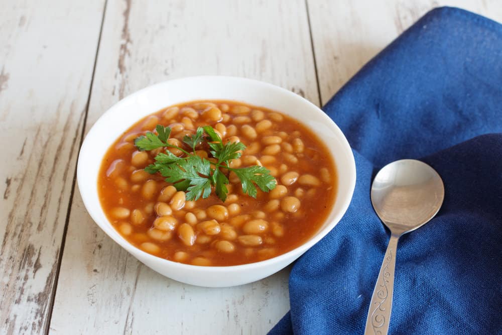 A white porcelain bowl filled with a steaming hot and flavorful combination of red kidney beans and tomato sauce.