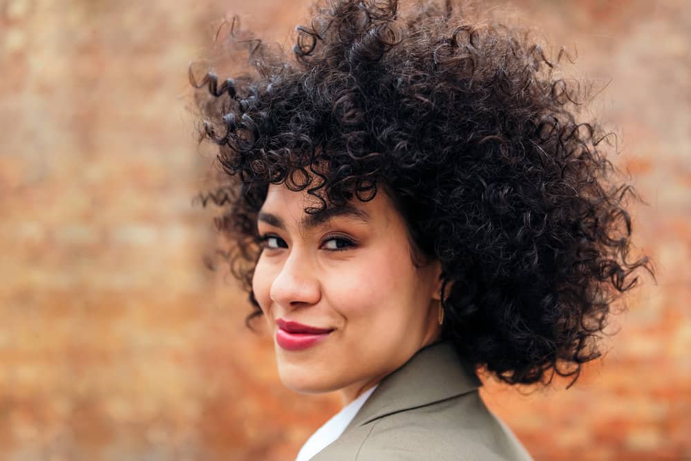 A young Latin female with thick hair used a boar bristle hair brush to style her type 3 curly hair strands.