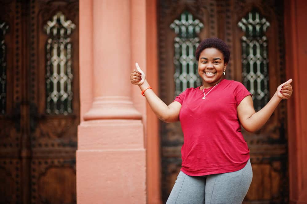 A young African American female with a beautiful style wearing a red t-short and gray jogging pants.