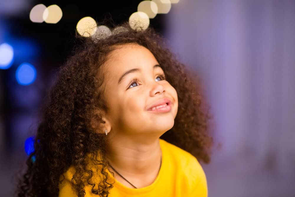 An adorable little girl's hair is styled in a naturally curly hairdo, which is a fun toddler girl hairstyle that's timeless.