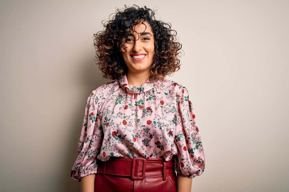 An Arab woman with a curly hair texture has pretty caramel highlights complimenting her rose gold skin tone.