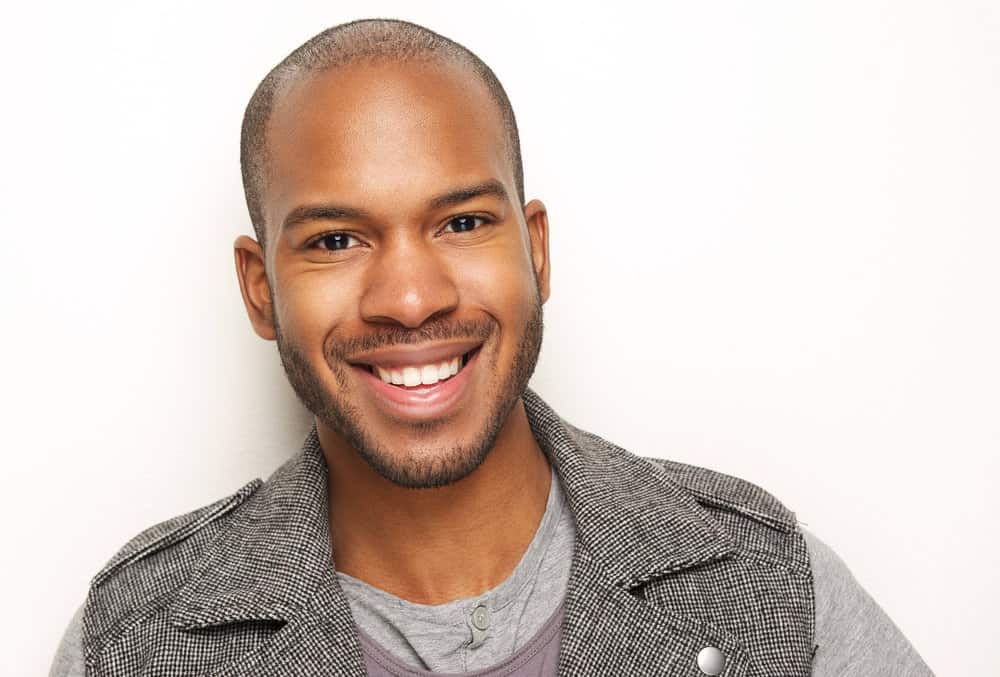 A stylish and bold African American man with a mid-bald fade has short hair after getting a buzz cut.