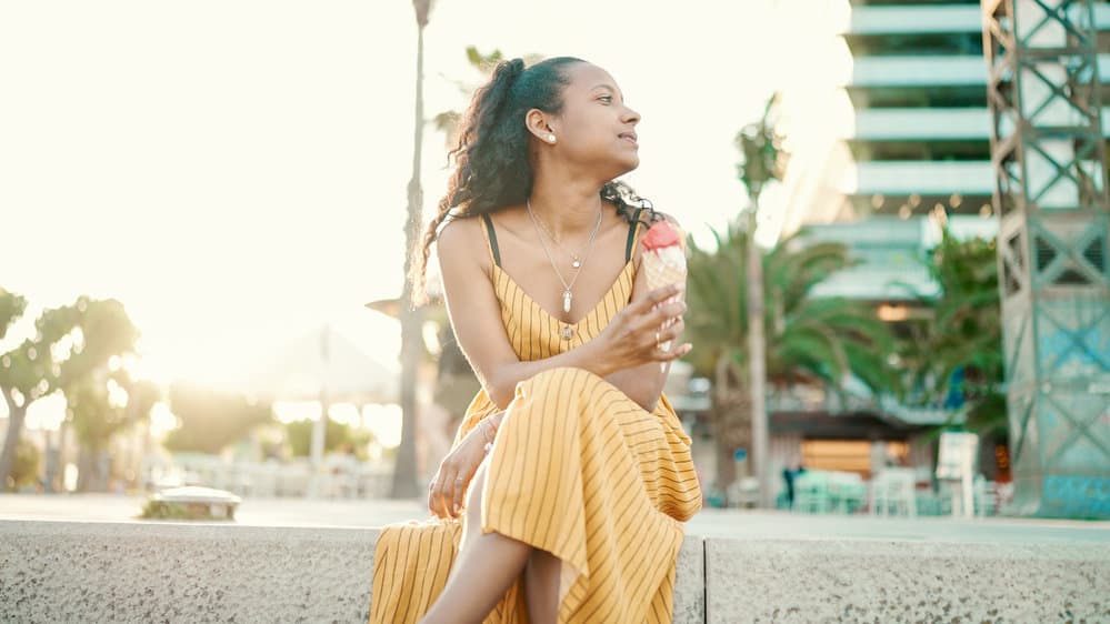 A cute urban girl in the city eating ice cream has long hair that was treated with rice water hair treatments.