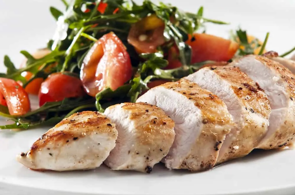 A grilled chicken breast served with leafy green vegetables.