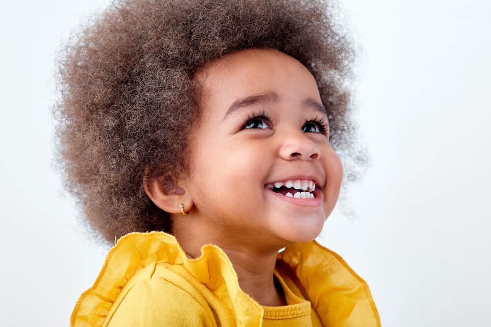 An adorable black baby wearing an afro hairstyle with a type 3 natural hair type creates an adorable look.