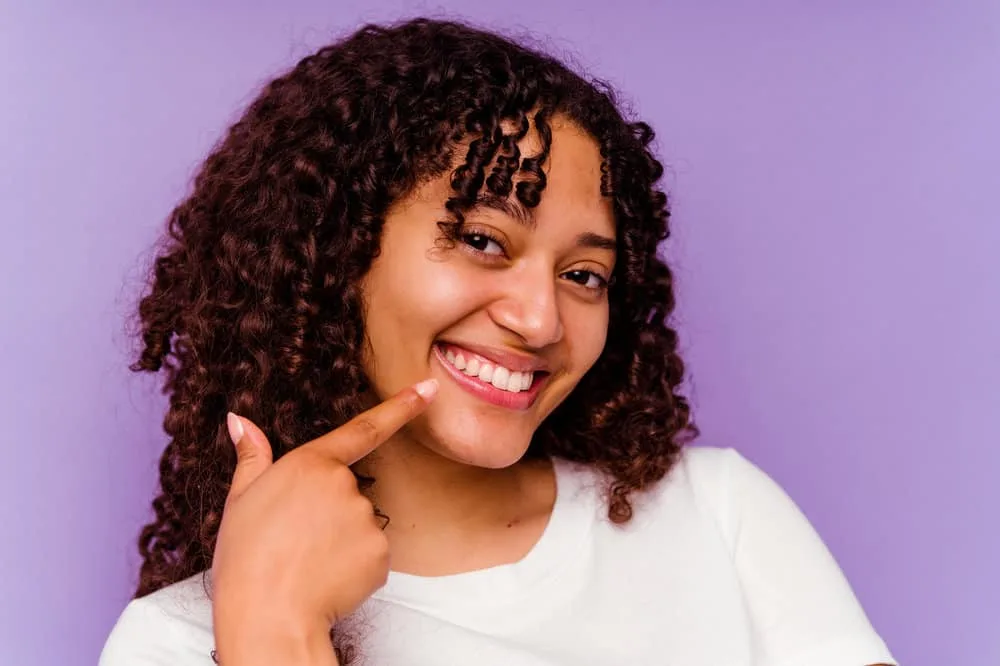 Women with curly hair looking in the camera holding her chin preparing to use a rosemary oil hair growth recipe.