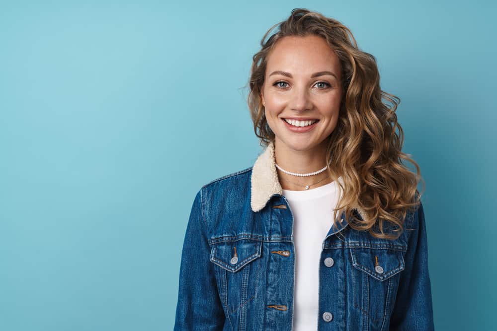 A beautiful white female with a warm butterscotch hair color is wearing a casual blue jean jacket and a white t-shirt.