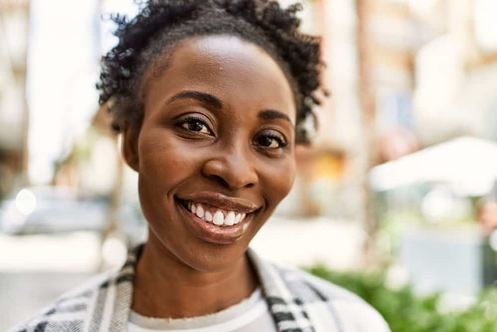 A lady with dark brown skin is wearing natural curls colored with henna dyes with synthetic chemicals.