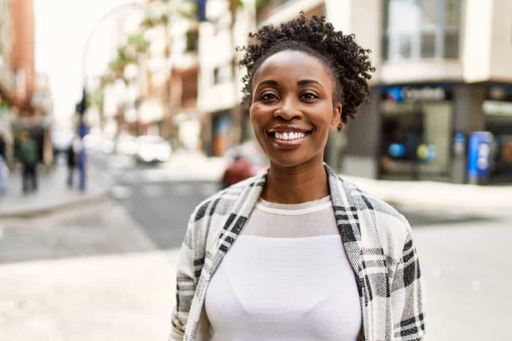 A stunning black woman is beaming with confidence as she flaunts her natural curls treated with a moisturizing mask.