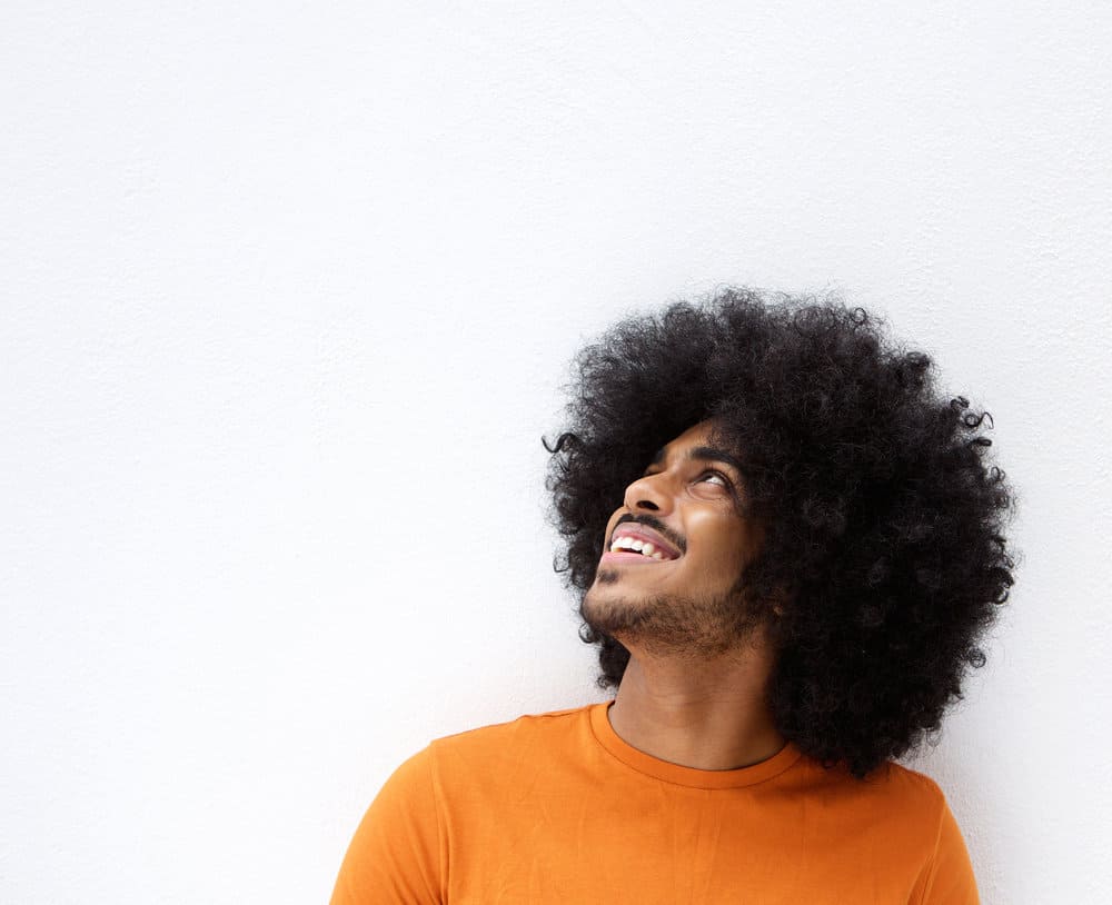 A smiling black man with afro hair grows quickly due to using a hair regimen designed specifically for black men's hair.