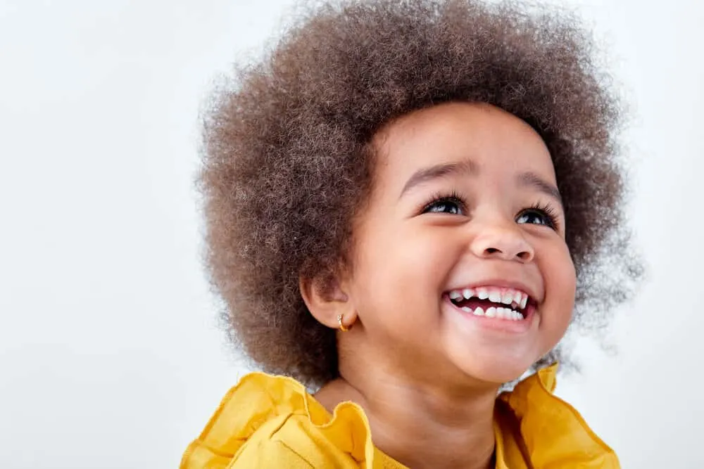 7 Cute & Easy Infant Black Baby Girl Hairstyles with Tutorials 15 A sweet baby girl with a big smile and a beautiful afro hairstyle gently styled with hair gel by a new mother.