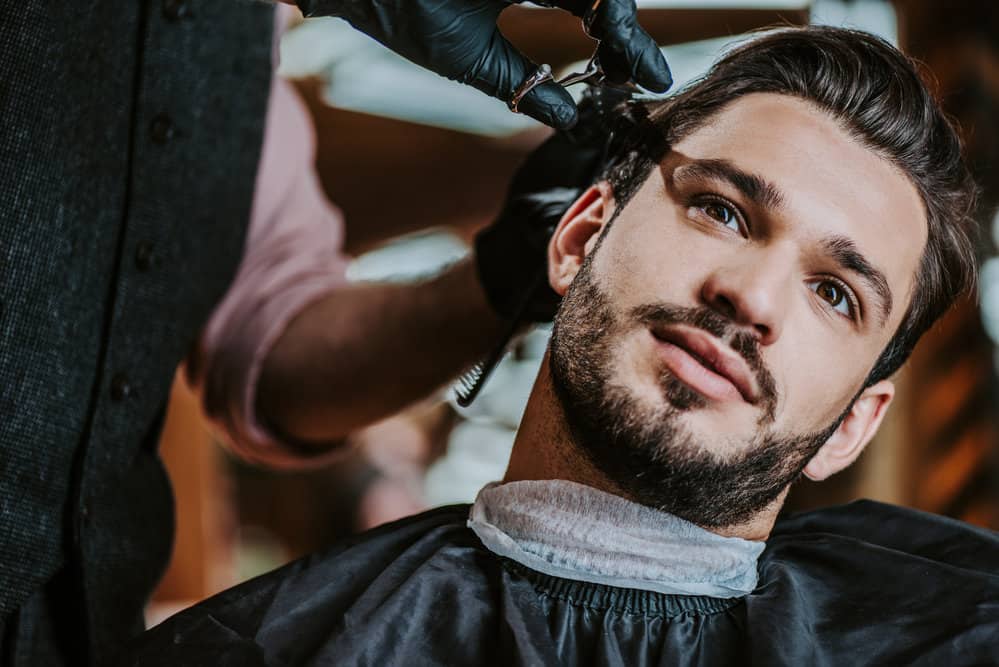 A barber creates a tight Edgar haircut on a man with a high-skin fade on the side and polishes it off with scissors.