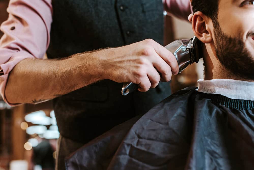 The barber uses Wahl clippers to bring a new look to his client's shoulder hair length with a bald fade Edgar haircut.