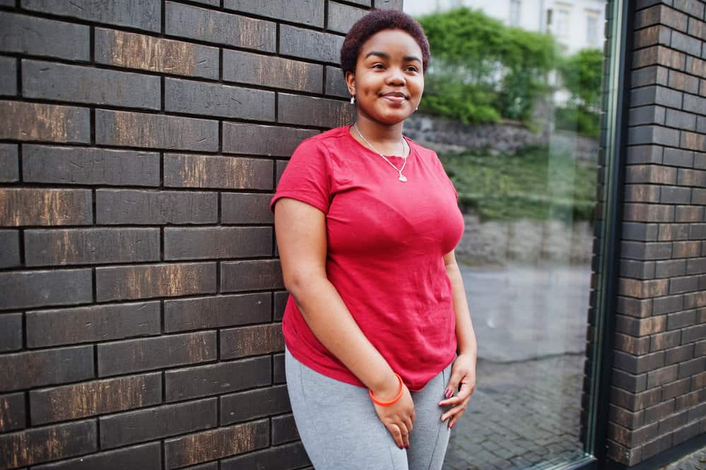 A black lady with a classic hairstyle with red highlights is wearing casual clothes as she leaves the local hair salon.