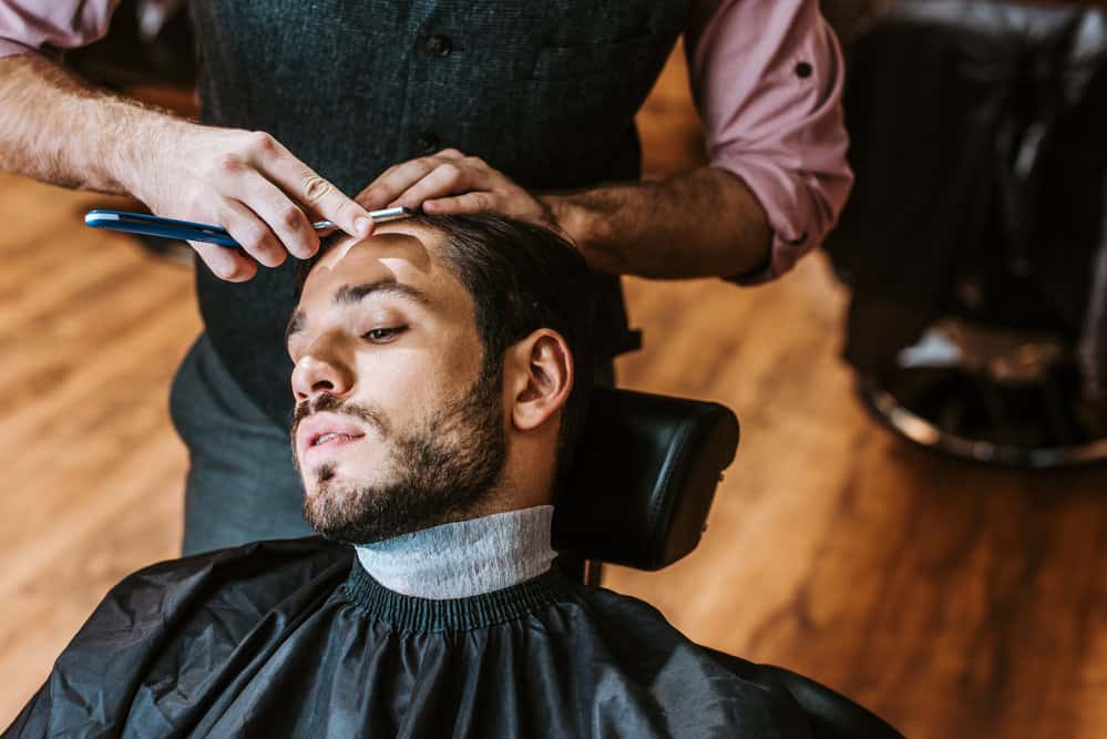 12 Different Edgar Cut Styles With Step-By-Step Tutorials 7 A barber works their magic on the type 1 hair texture of a Caucasian man, giving him a classic Edgar haircut.