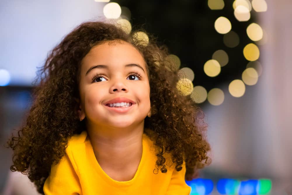 A sweet African American young girl shows off her curly tresses after undoing pig-tails on her type 3 dry hair.