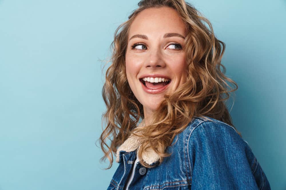 A happy young woman with medium-brown curls with dark roots and chestnut brown undertones.