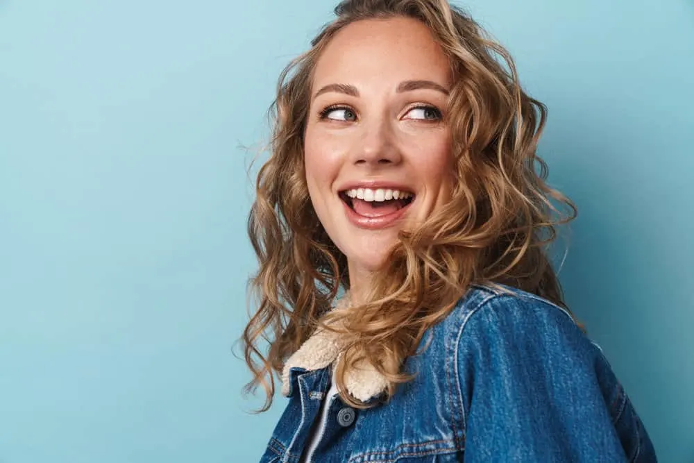 How to Get Butterscotch Hair Color and What Does It Look Like 6 A happy young woman with medium-brown curls with dark roots and chestnut brown undertones.