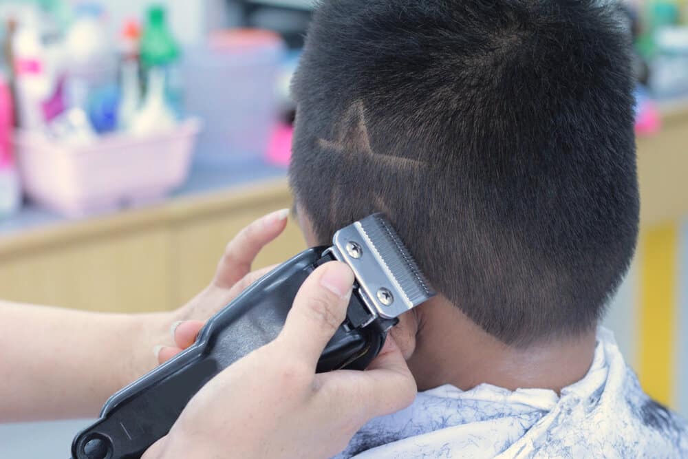 A little boy with straight hair is getting a double-line haircut with sharp edges on his naturally short hair.