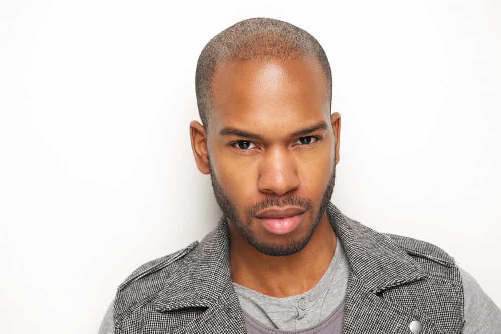 An African American man with thin hair and a receding hairline wearing a taper fade and a thick beard.