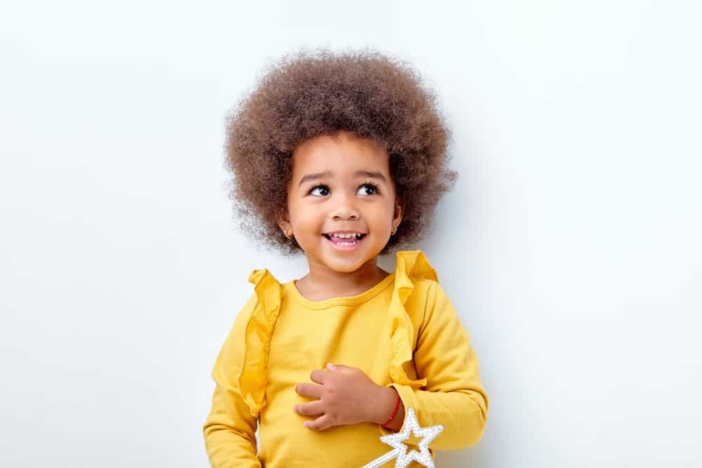 An adorable baby daughter with a cute hairstyle and an infectious smile on her curly black hair strands.