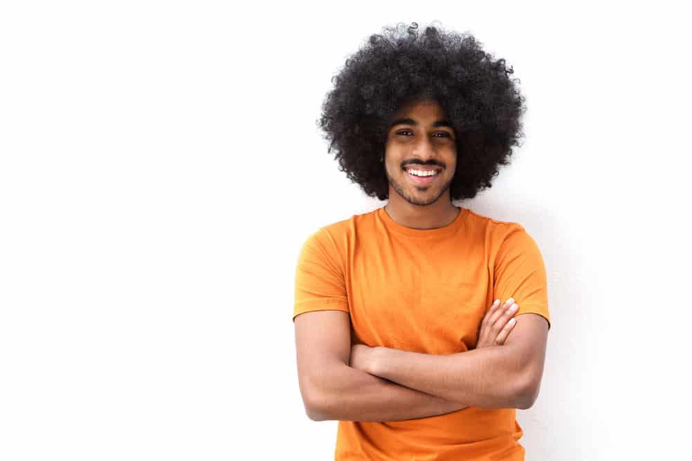 A black guy with a great smile uses a weekly scalp massage and eats green leafy vegetables to boost hair growth. 