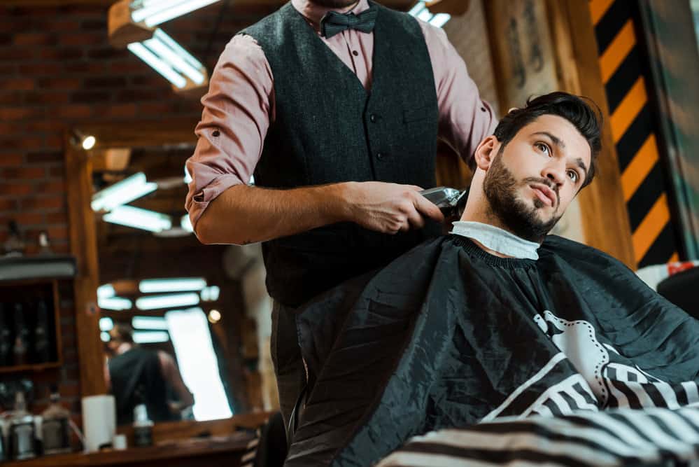 12 Different Edgar Cut Styles With Step-By-Step Tutorials 22 A barber using brand-new Wahl hair trimmers works their magic on a man's hair, creating an Edgar haircut bald fade.