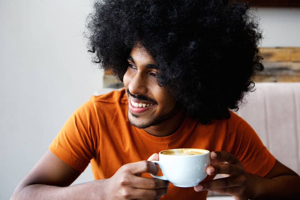 A handsome African man showing off his luscious locks after a scalp massage routine to improve hair growth.