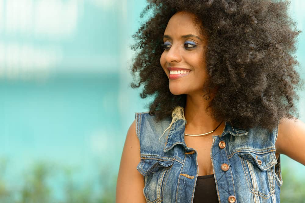 A black girl with silky light brown skin has an outer-layer hair strand and cuticle layer damaged from heat styling tools.