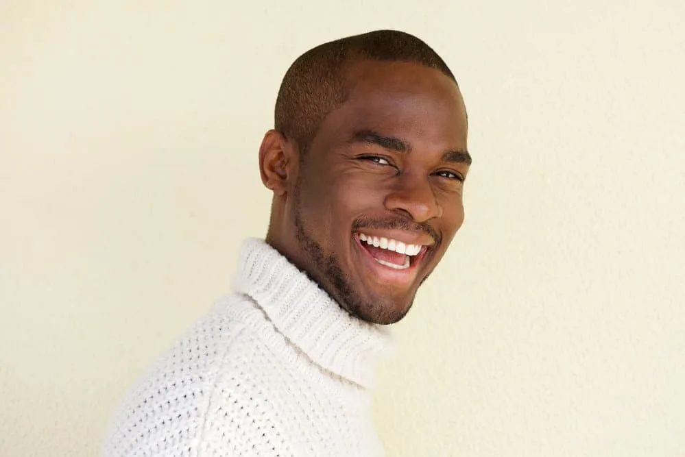 A stylish black dude with a short hair length created with a low guard clipper wearing a fashionable sweater.
