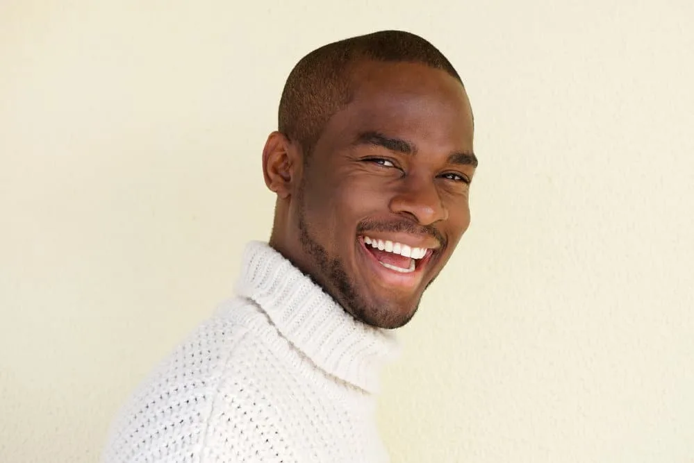 8 Types of Military Buzz Cut Fade Styles, Designs, and Ideas 10 A stylish black dude with a short hair length created with a low guard clipper wearing a fashionable sweater.