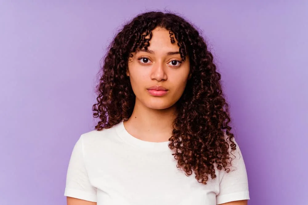 A mixed race female looking directly into the camera wearing red lipstick, eye shadow and a white tank top.