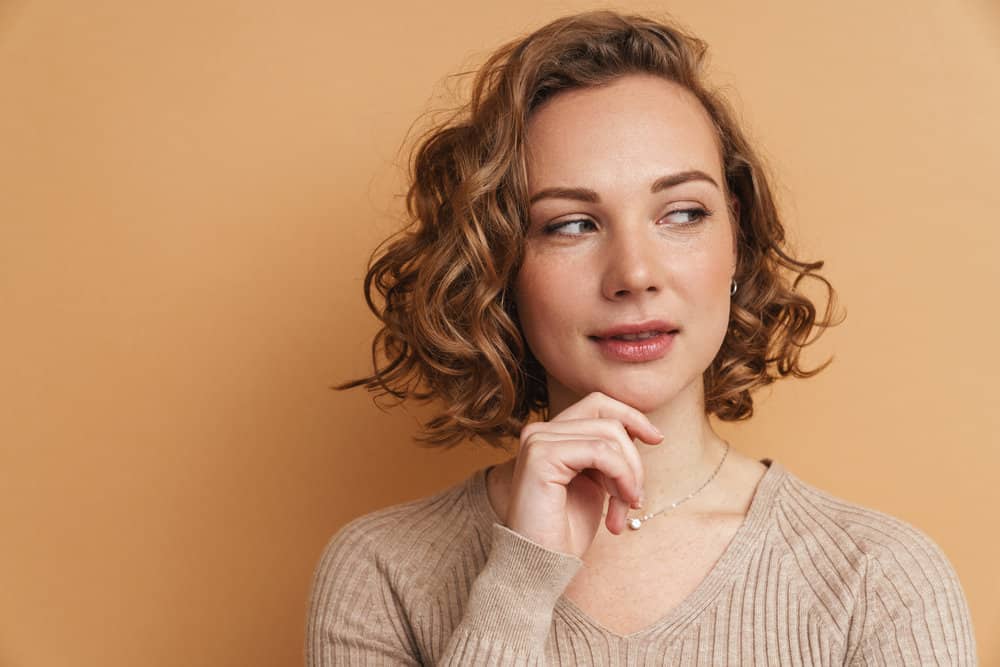 A cute white female with cascading shoulder-length hair is delicately swept to the side with her type 2 hair texture.