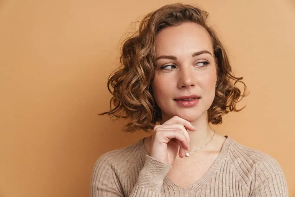 12 Best Medium-Length Haircuts With Layers, Bangs, & More 2 A cute white female with cascading shoulder-length hair is delicately swept to the side with her type 2 hair texture.