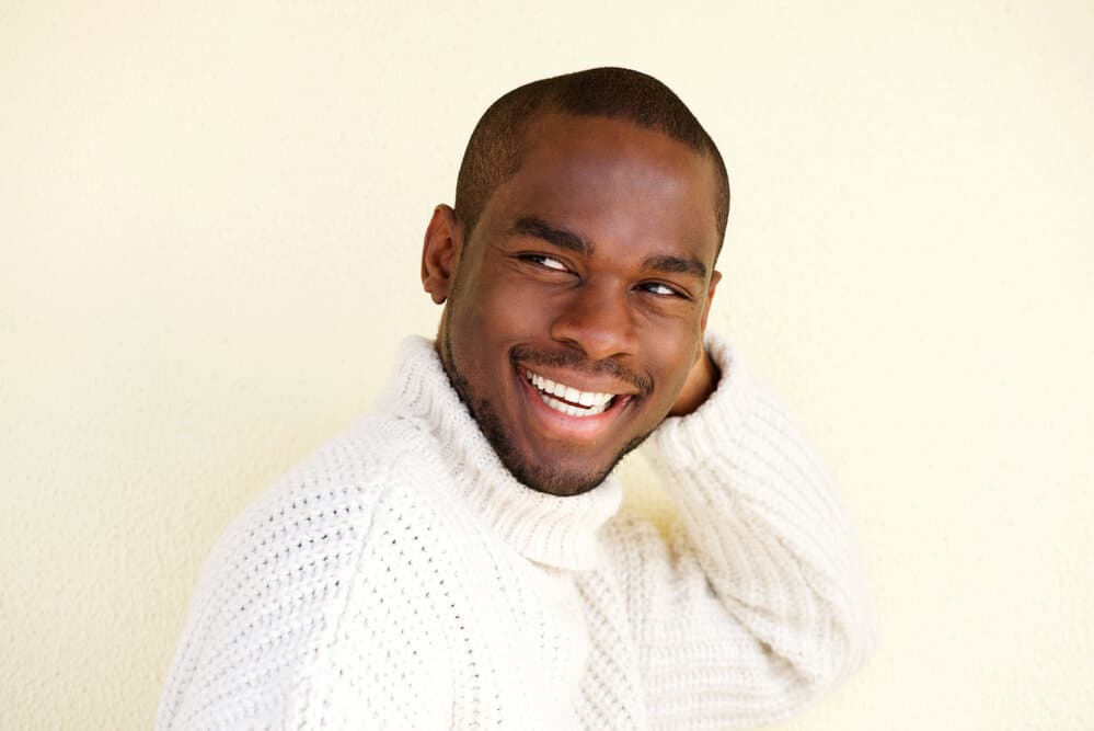 A stylish young black dude with a low-fade haircut created with electric hair clippers wears a stylish sweater.