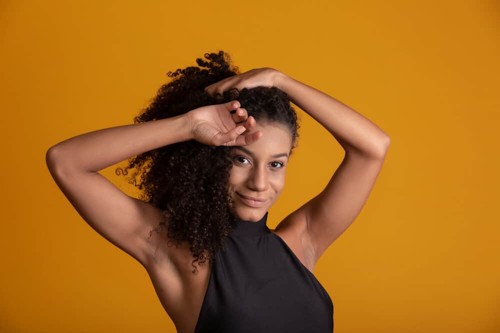 A charming black girl with dark brown hair has short curly hair on a collarbone razored feathered bob hairstyle.