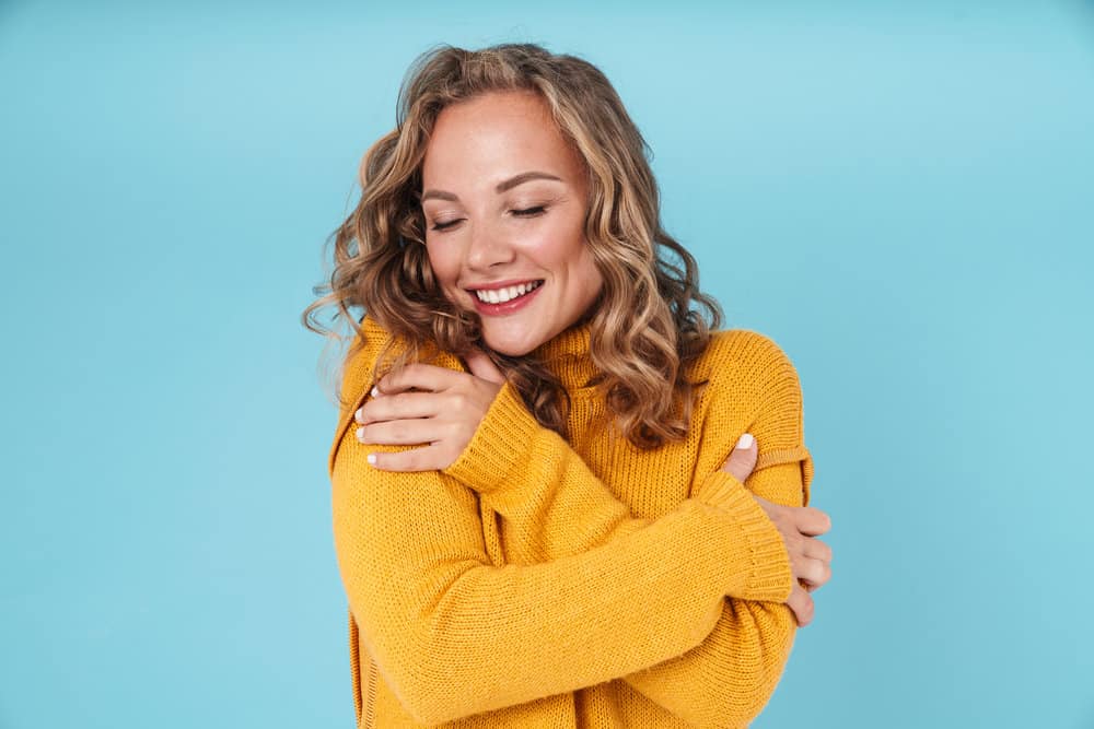 A Caucasian woman with voluminous curls keeps her hair hydrated with hair creams and water-based styling products.