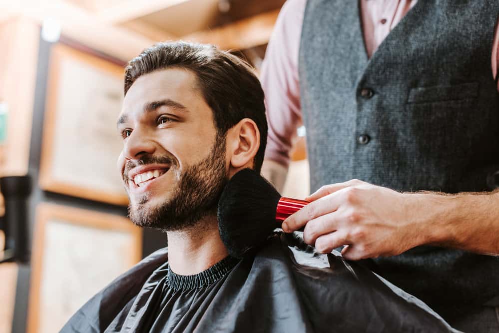 A male sits in the barber's chair that's ready for a makeover and is discussing Edgar haircuts and styles with his barber.