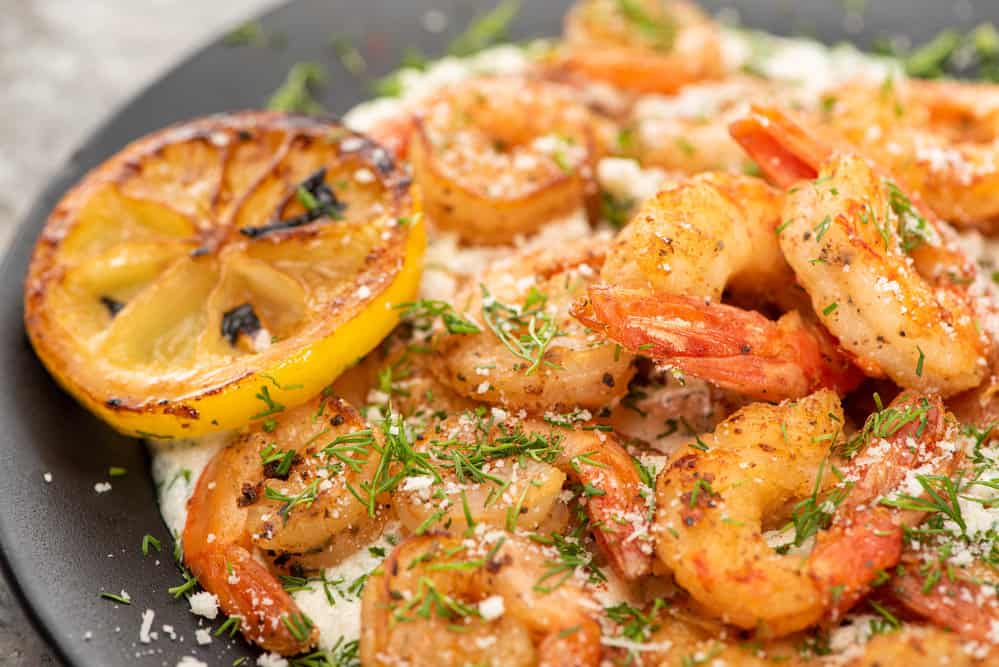 A delicious meal consisting of cooked pink shrimp and grits on a plate in a dimly lit restaurant setting.