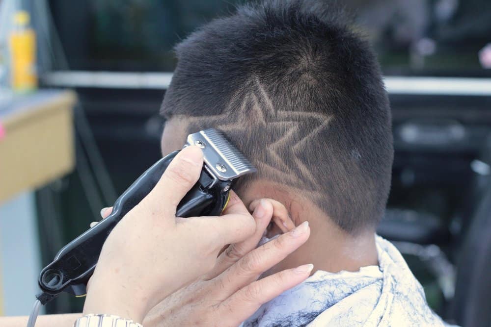 This young boy's wavy hair is transformed with thin lines and haircut designs, giving it a sleek and edgy look.