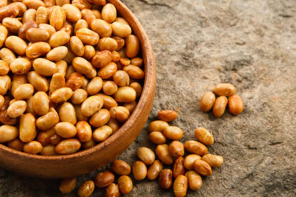 A pile of fresh, uncooked soybeans with their fuzzy brown pods spilling out, showcasing the varying shades of brown.