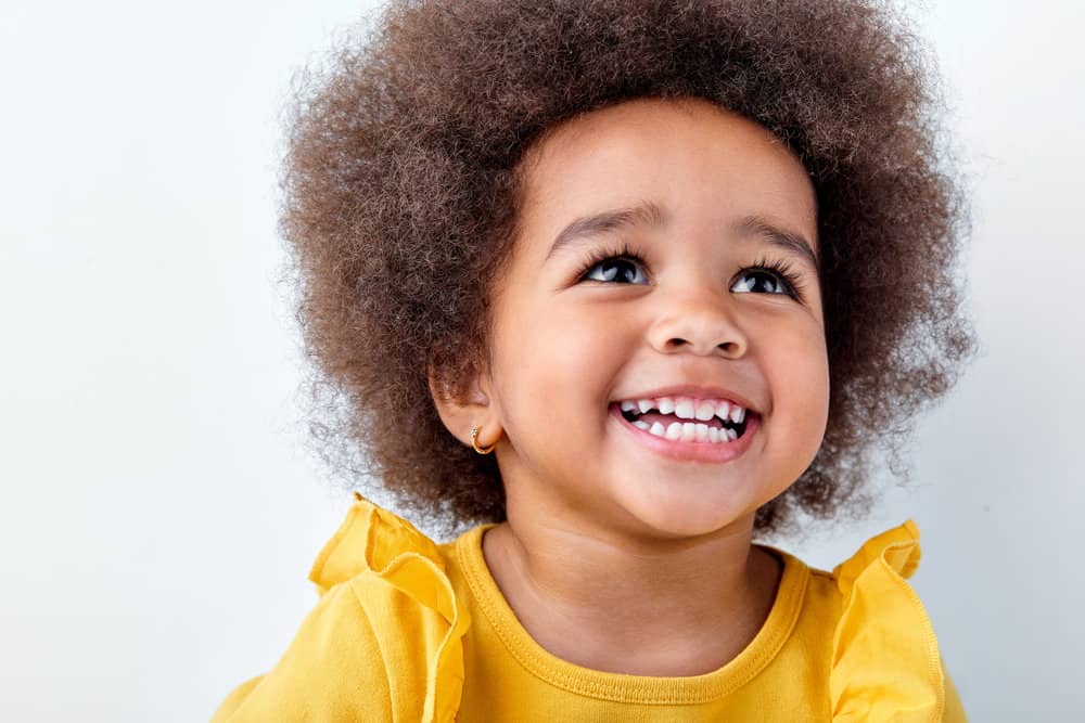 A cute baby of color with a type 3 natural hair type, wearing a stylish headband to complete the look.