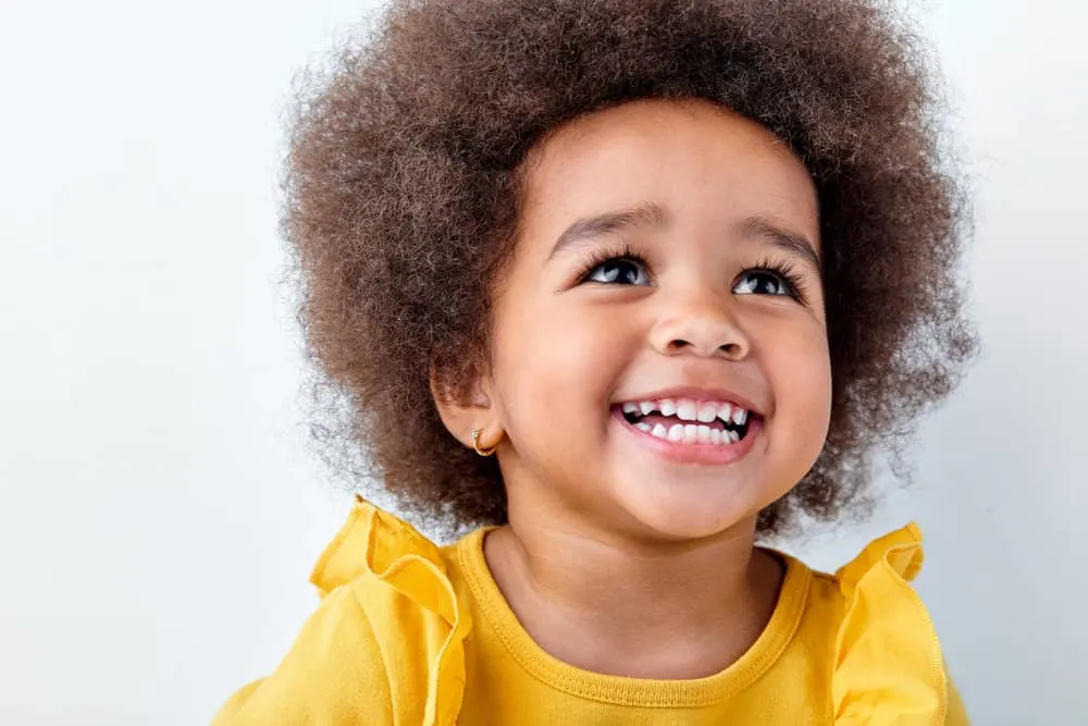 7 Cute & Easy Infant Black Baby Girl Hairstyles with Tutorials 6 A cute baby of color with a type 3 natural hair type, wearing a stylish headband to complete the look.
