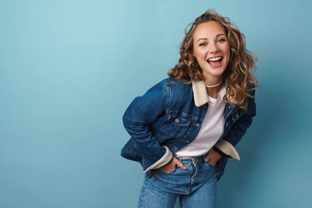 A stylish young white woman wearing a curly auburn brown butterscotch hairdo with ash blonde undertones.